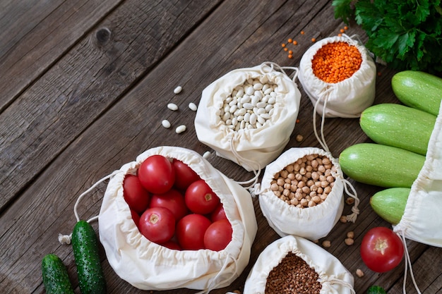 Sacos de mantimento de matéria têxtil com aveia em flocos e legumes frescos na tabela de madeira em cima. refeição doar ou conceito de suprimentos alimentares