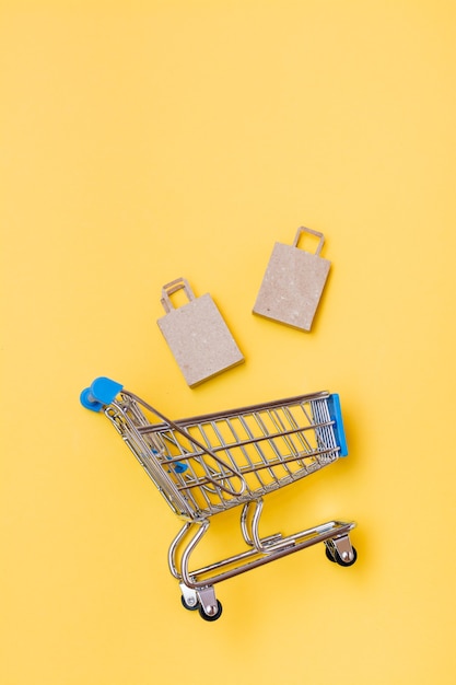 Foto sacos de papel artesanal ecológicos caem em um carrinho de compras de metal sobre um fundo amarelo. black friday, venda de presentes. vista superior e vertical