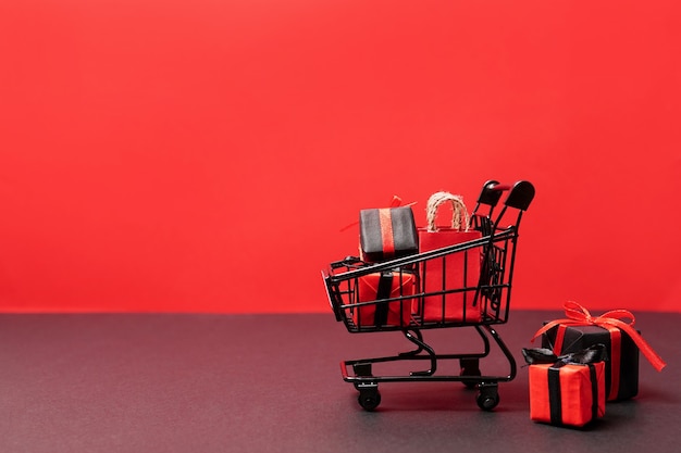 Sacos de papel pretos e caixas de presente no carrinho de compras em vermelho