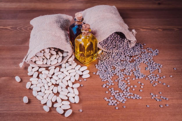 Sacos de frijoles y lentejas y una botella de aceite de oliva en una mesa de madera