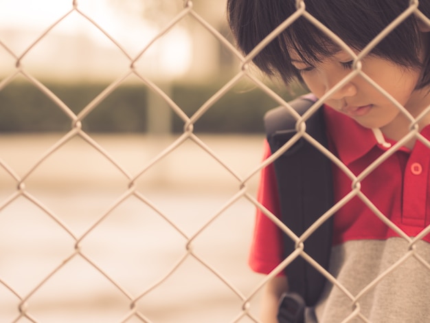 Sad Boy hinter Zaun Mesh Netting. Emotionen-Konzept.