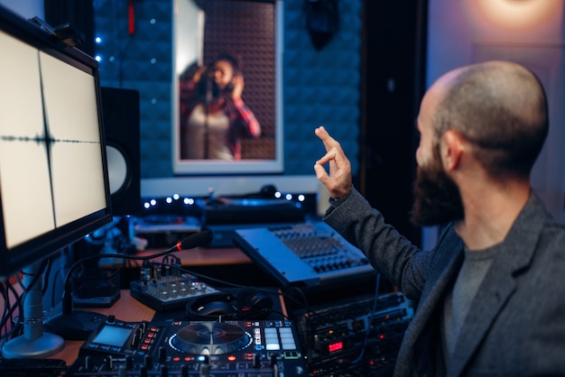 Sängerin im Aufnahmeraum und Tontechnikerin und am Fernbedienfeld im Studio.