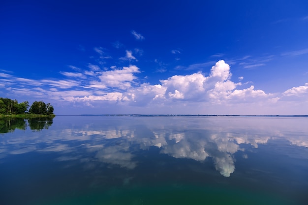 Säubern Sie den blauen Himmel, der im ruhigen Wasser am Sommertag reflektiert wird