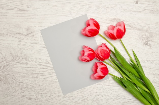 Säubern Sie graues Blatt Papier und rosa Tulpen auf einem hellen Holztisch