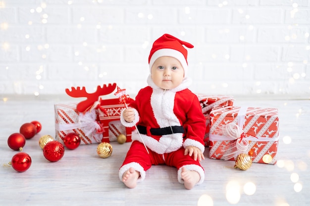 Säuglingskind im roten Sankt-Kostüm sitzt mit Geschenken auf weißem Hintergrund des neuen Jahres Weihnachtsferien