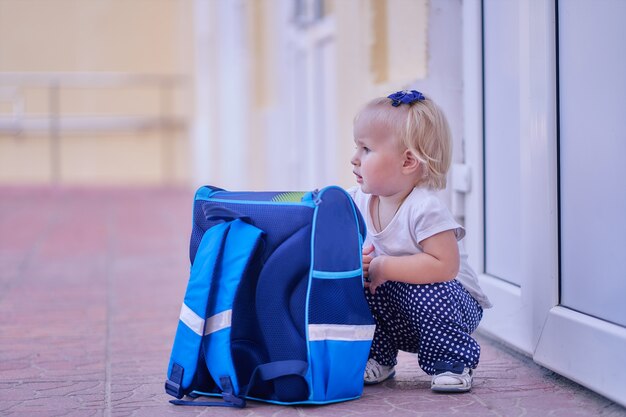 Foto säuglingsmädchen mit einer schultasche sitzt am schulkopierraum