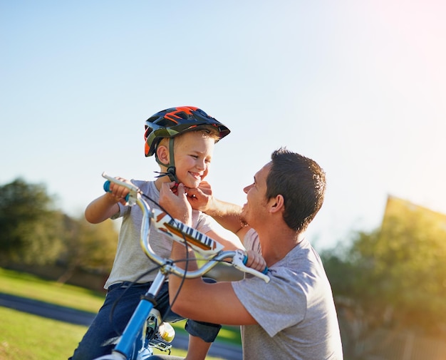 Safety first son Aufnahme eines Vaters, der seinem Sohn einen Helm aufsetzt, während er ihm das Fahrradfahren im Park beibringt