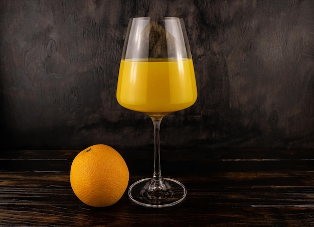 Saft in einem Glas und einer Orange auf dunklem Holzhintergrund