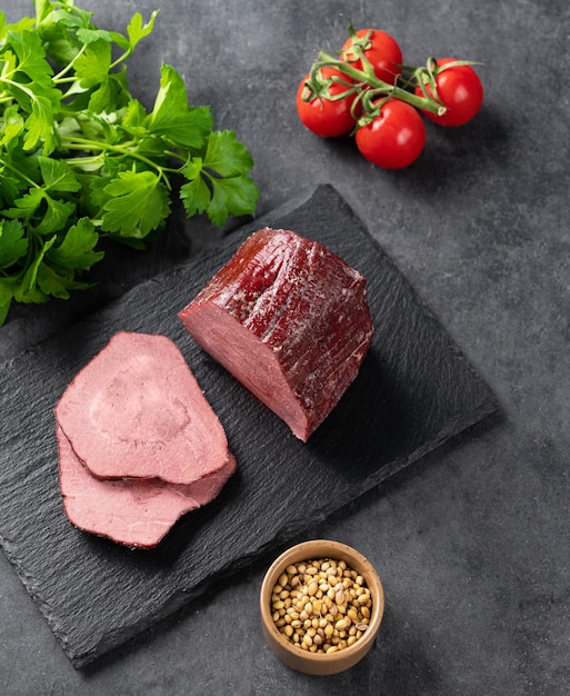 Saftig gebackenes Roastbeef auf einem Schieferbrett mit Tomaten und frischen Kräutern auf dunklem Hintergrund