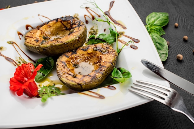 Saftige gegrillte Avocado mit Sauce und Kräutern auf Holzhintergrund