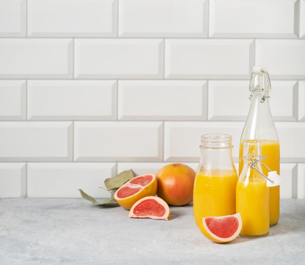 Saftige Grapefruit und abgefüllter Saft auf einem blauen Tisch auf weißem Backsteinhintergrund Vorderansicht und Kopierbereich