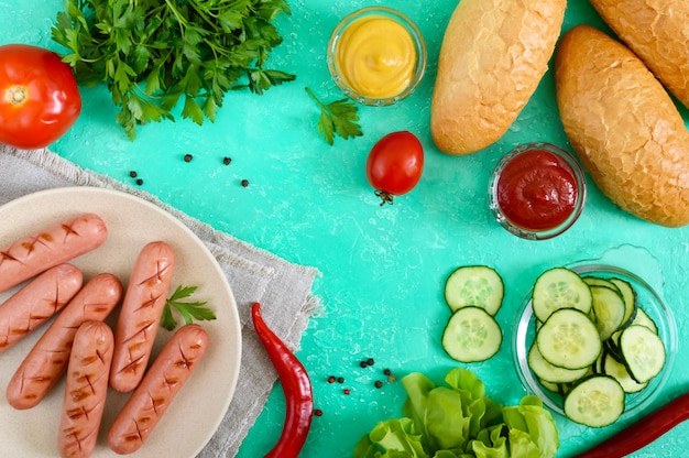Saftige Grillwürste, frisches Gemüse, Gemüse und knusprige Brötchen. Draufsicht. Zutaten für Hot Dogs. Flach liegen.