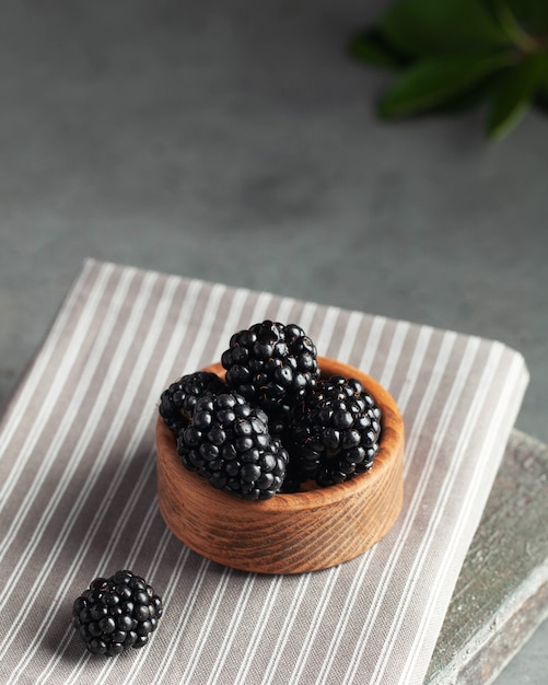 Saftige reife Brombeeren auf einem Holzteller auf einem grauen Tisch