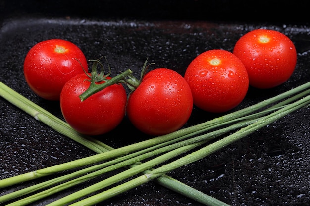 Saftige süße rote Tomaten und grüne Zweige auf schwarzem Hintergrund Gesundes Ernährungskonzept Nahaufnahme