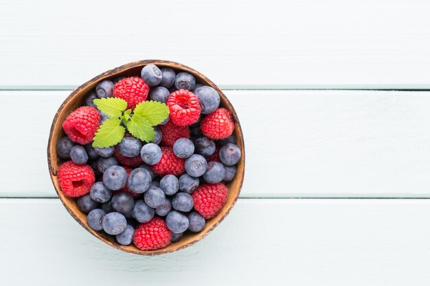 Saftige und frische Blaubeeren mit grüner Minze auf rustikalem blauem Tisch.