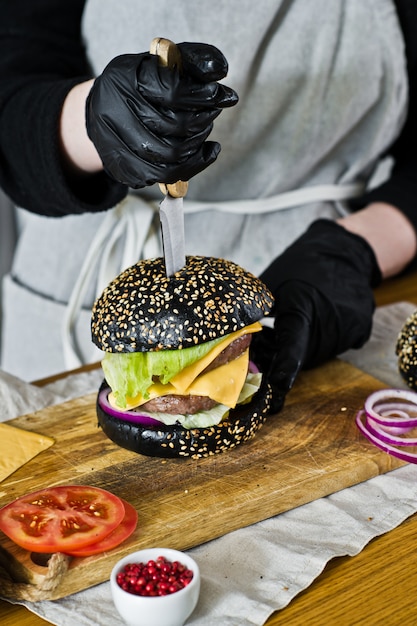 Saftiger Burger in den Händen des Chefs. Das Konzept des Kochens des schwarzen Cheeseburgers. Selbst gemachtes Hamburgerrezept