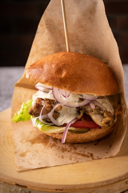 Saftiger Fleischburger mit frischem Gemüse und Gewürzen. weiches duftendes Brötchen und natürliche Saucen. Seitenansicht. auf dunklem Hintergrund, für Menüs und Anzeigen