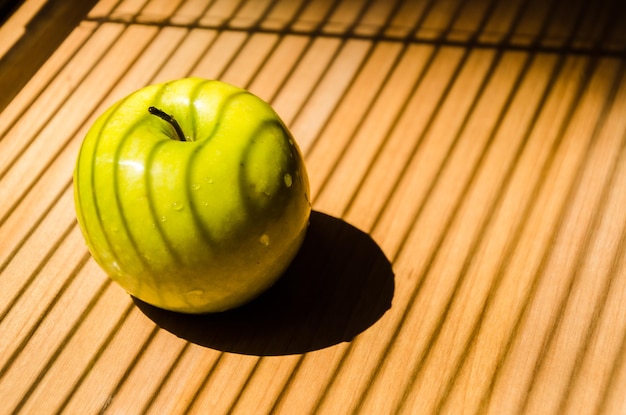 Saftiger grüner Apfel mit Wassertropfen auf der Fensterbank Licht und Schatten von Jalousien Gestreifte Schatten