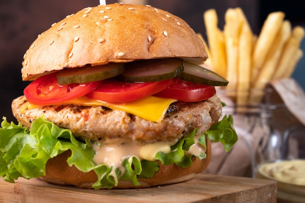 Saftiger Hühnerburger mit eingelegten Gurken und Tomaten, Nahaufnahme und Pommes.