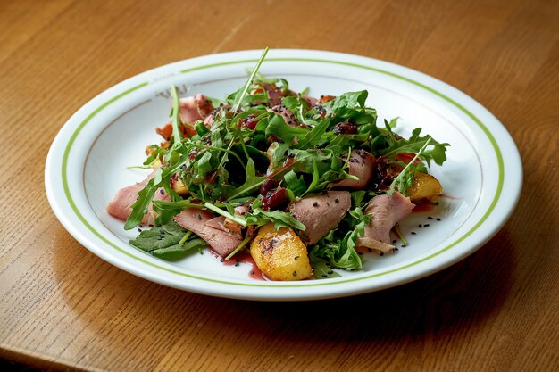 Saftiger Salat mit geräucherter Ente, Pfirsich und Rucola in einem weißen Teller