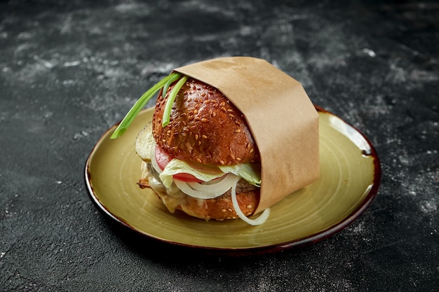 Saftiger und appetitlicher Burger mit Rindfleisch, Salat, Mozzarella und Tomaten auf einem Vintage-Teller auf einem Holztisch. Nahaufnahme, selektiver Fokus. Rauschkorn auf dem Pfosten hinzugefügt