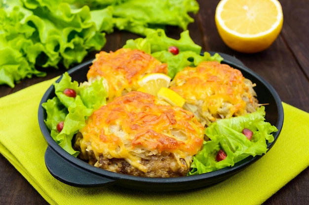 Saftiges Fleischkotelett, gebacken mit geriebenen Kartoffeln und Käse auf einer gusseisernen Pfanne auf einem dunklen Holztisch. Nahansicht