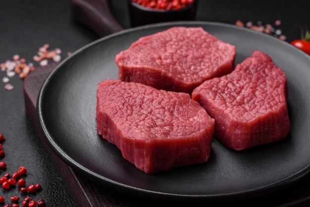 saftiges frisches rohes Rindfleisch mit salzigen Gewürzen und Kräutern auf einem dunklen Beton-Hintergrund