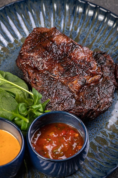Saftiges gegrilltes Stück gegrilltes Steak mit Spinat und Saucen auf einem glänzenden blauen Teller Ein herzhaftes Gourmet-Mittagessen Einfache Idee für ein traditionelles Mittagessen Restaurantversorgung