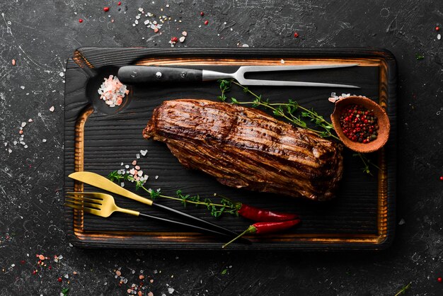 Saftiges Kalbssteak mit Gewürzen auf einem schwarzen Holzbrett. Ansicht von oben. Gegrilltes Fleisch.