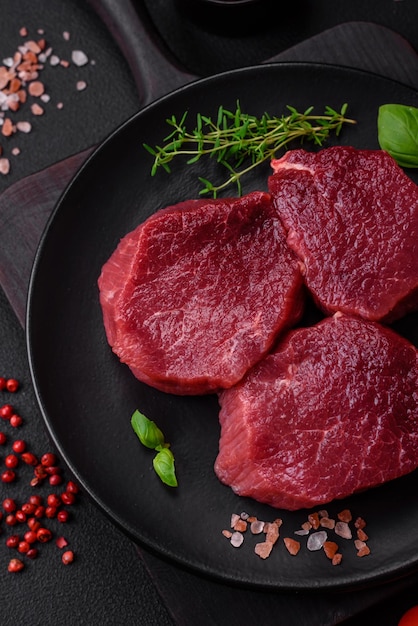 Saftiges rohes Rindfleisch mit Gewürzen, Salz und Kräutern auf dunklem Betongrund