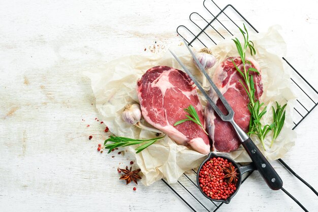 Saftiges rohes Steak mit Gewürzen auf einem weißen Tisch. Ribeye-Rindersteak. Ansicht von oben. Freiraum für Ihren Text.