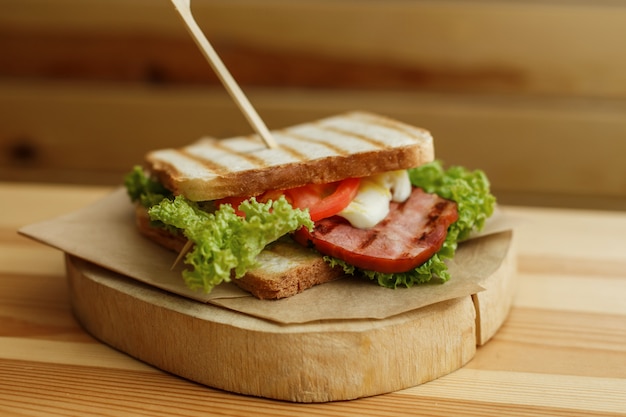 Saftiges Sandwich mit gegrilltem Brot und Speck warten auf Sie auf hölzerner Platte