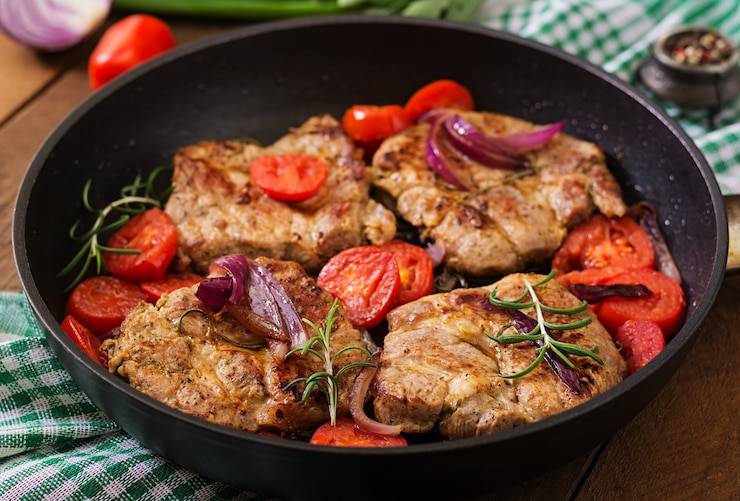 Foto saftiges schweinesteak mit rosmarin und tomaten auf pfanne