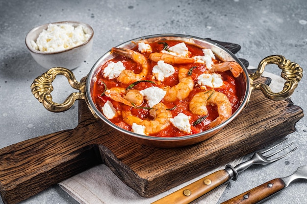 Saganaki de langostinos al horno tradicional griego con queso feta, tomate, pimentón y tomillo. fondo gris. Vista superior.