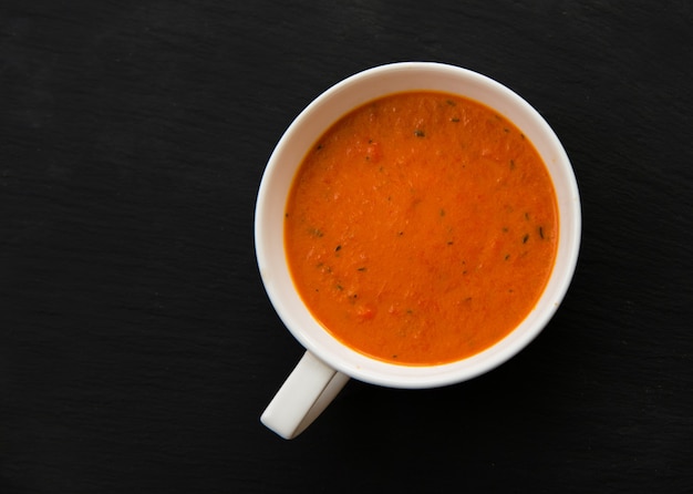 Sahnesuppe mit gerösteten Paprika und Tomaten auf schwarzem Teller, Draufsicht