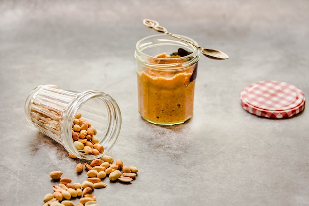 Sahnige und glatte Erdnussbutter im Glas auf grauer Tabelle.