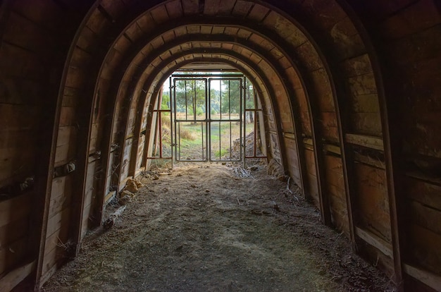 Saída abandonada da mina, túnel subterrâneo com paredes de madeira, barras de ferro e vista externa