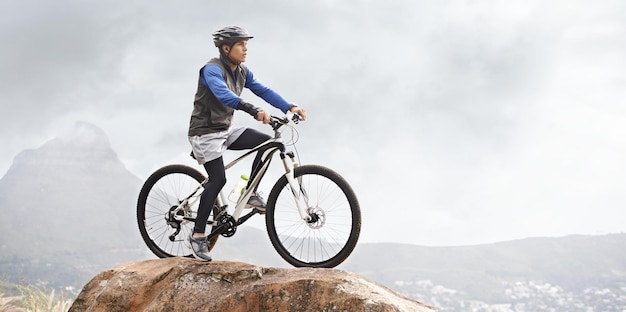 Saindo para um passeio de mountain bike Um jovem em uma mountain bike com uma vista deslumbrante ao fundo