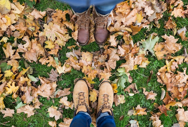 Saison- und Menschenkonzept - ein paar Füße in Stiefeln mit Herbstblättern auf dem Boden