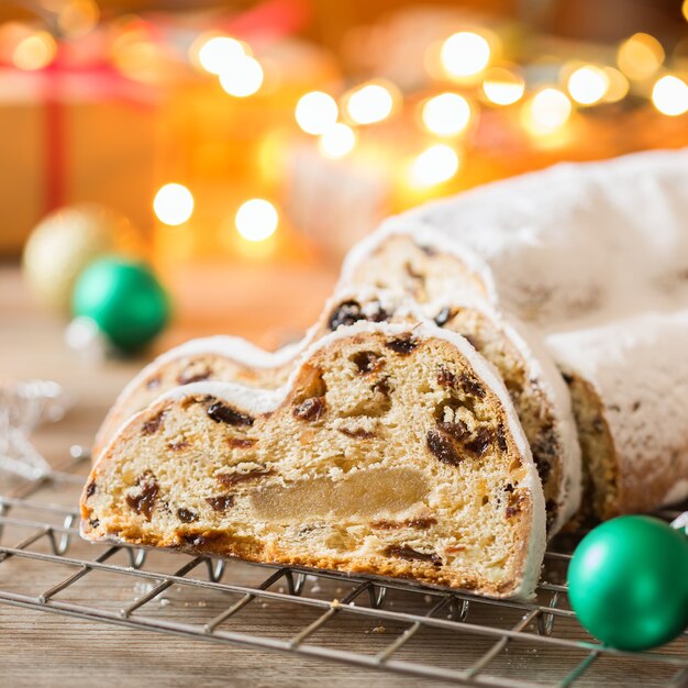 Saisonale Speisen und Getränke, Winterkonzept. Traditioneller europäischer deutscher hausgemachter Weihnachtskuchen, Gebäckdessert Stollen auf einem hölzernen Hintergrund mit festlicher Dekoration.