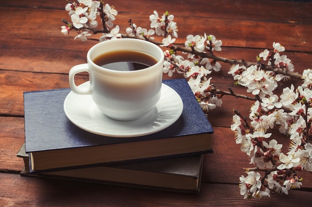 Sakura ramos com flores, copo branco com café preto e dois livros sobre uma superfície de madeira escura. Conceito de primavera