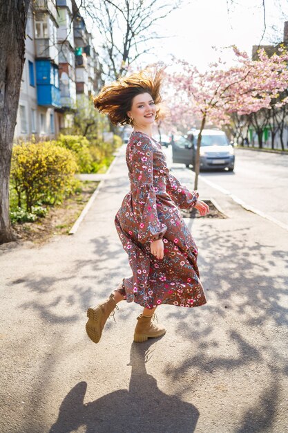 Sakura verzweigt sich mit Blumen an einem Baum in den Straßen der Stadt. Glückliches Frauenmädchen, das sich mit blühender Kirschblüte auf der Straße dreht. Sakura-Blüten.