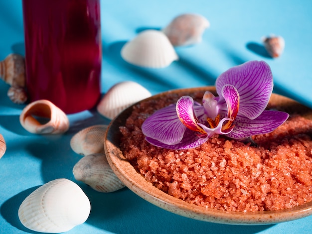 Sal de baño naranja en un platillo con conchas, velas rojas y flores sobre un fondo azul con una sombra de una planta tropical. Copyspace Spa, relajado, verano