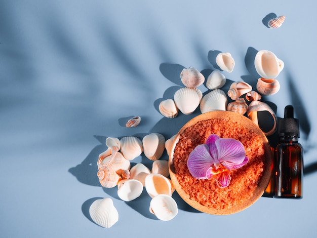 Sal de banho laranja em um pires com conchas e flores sobre fundo azul com uma sombra de uma planta tropical. Copyspace, flatlay. Spa, relaxado, verão