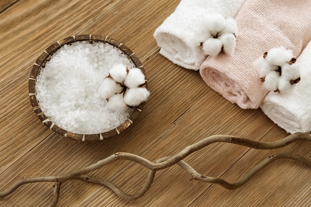 Sal do mar branco na tigela de coco natural e flores de algodão macio e toalhas de banho enroladas na superfície de madeira velha. ainda vida para o conceito de spa. copie o espaço e a vista superior.