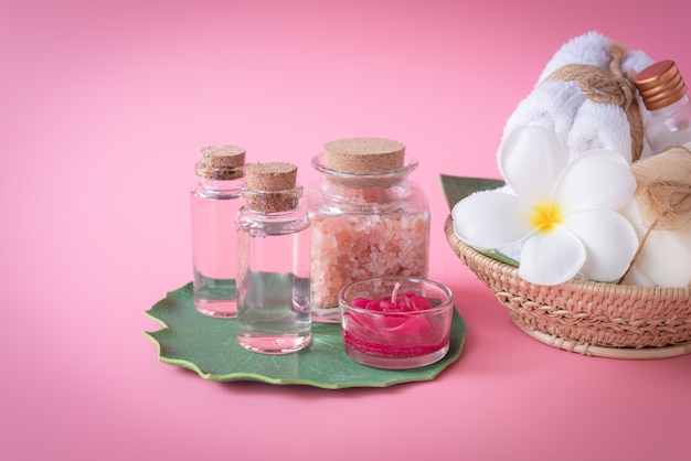 Sal de Himalaya Spa, vela roja, leche y jabón líquido de rosas, toalla blanca, flores sobre hojas verdes sobre rosa