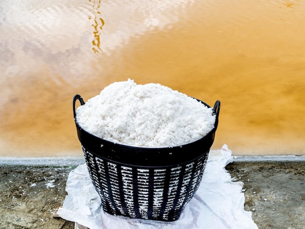 Sal marina blanca en cesta de plástico cerca de estanques de evaporación de sal Concepto de producción de proceso de sal de cultivo de sal