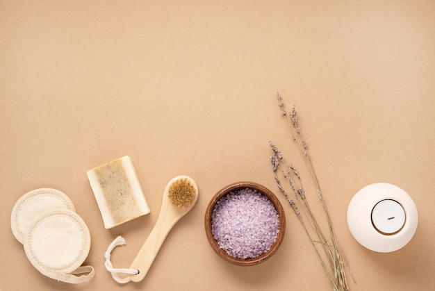 Sal marinho orgânico para o corpo com flores secas de lavanda escova de esponja sabão e vela em um fundo bege Cuidados com a pele O conceito de um produto de spa natural e ecológico Espaço de cópia de vista superior