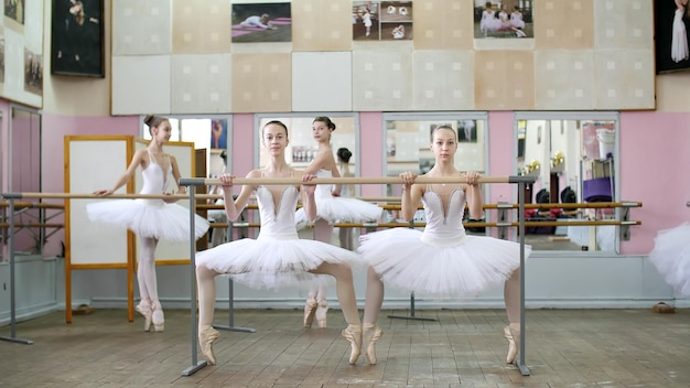 Foto en la sala de ballet las chicas en blancos paquetes de tutus de ballet están comprometidas en el ensayo de ballet plie adelante