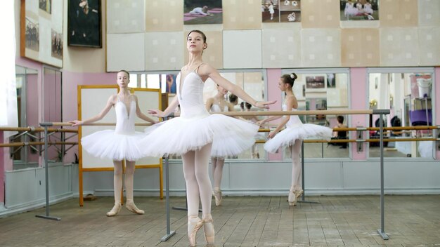 Foto en la sala de ballet las chicas con faldas de ballet blancas están comprometidas en el ensayo de ballet girando